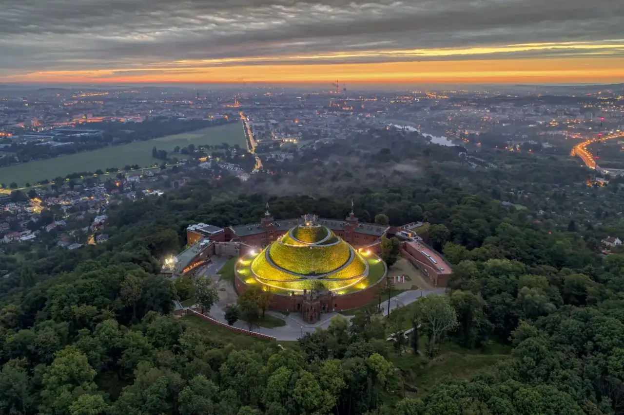 Kraków o wschodzie słońca, z górującym nad lasem, oświetlonym Kopcem Kościuszki.