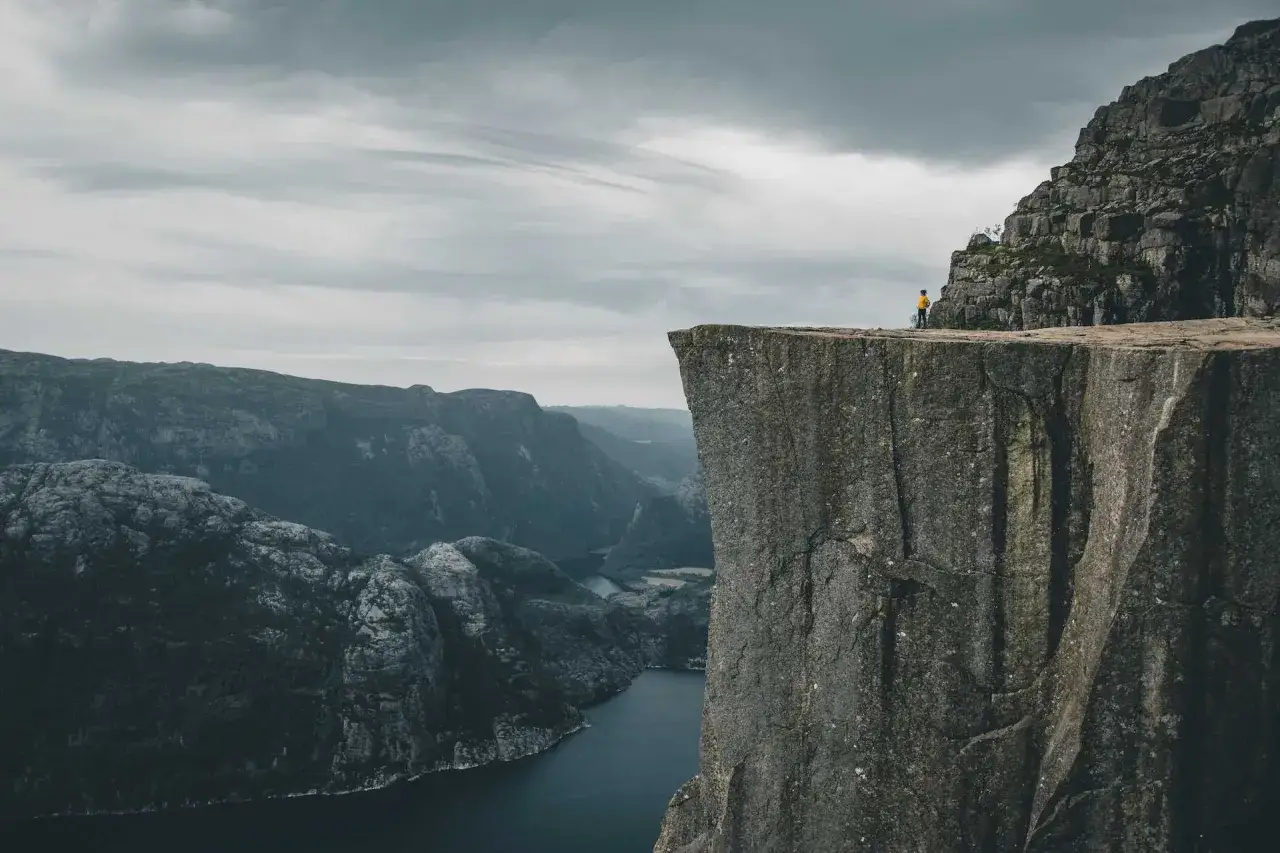 Widok z Preikestolen, jak dojechać do tego cudu natury. Człowiek na krawędzi klifu, w oddali fiord i góry.