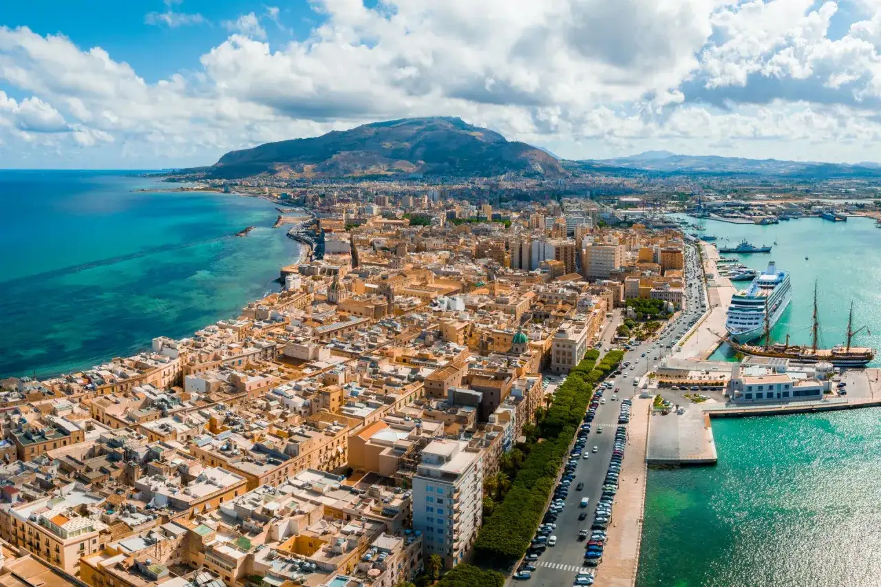 Widok na port i miasto na Sycylii. Czy to Trapani czy Palermo? Widać statki wycieczkowe i górzysty krajobraz w tle.