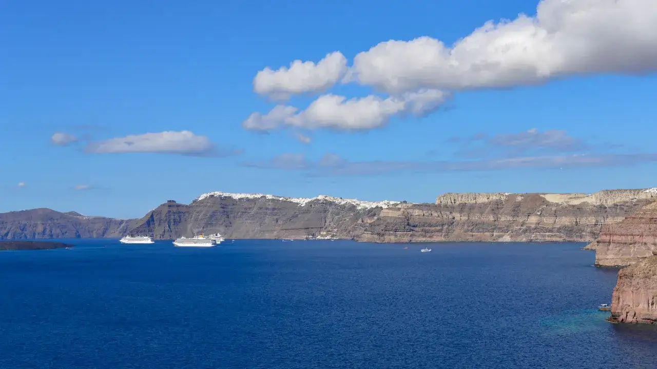 Widok na kalderę Santorini, Grecja. Białe domy wznoszą się na klifach, a po błękitnym morzu pływają statki wycieczkowe.