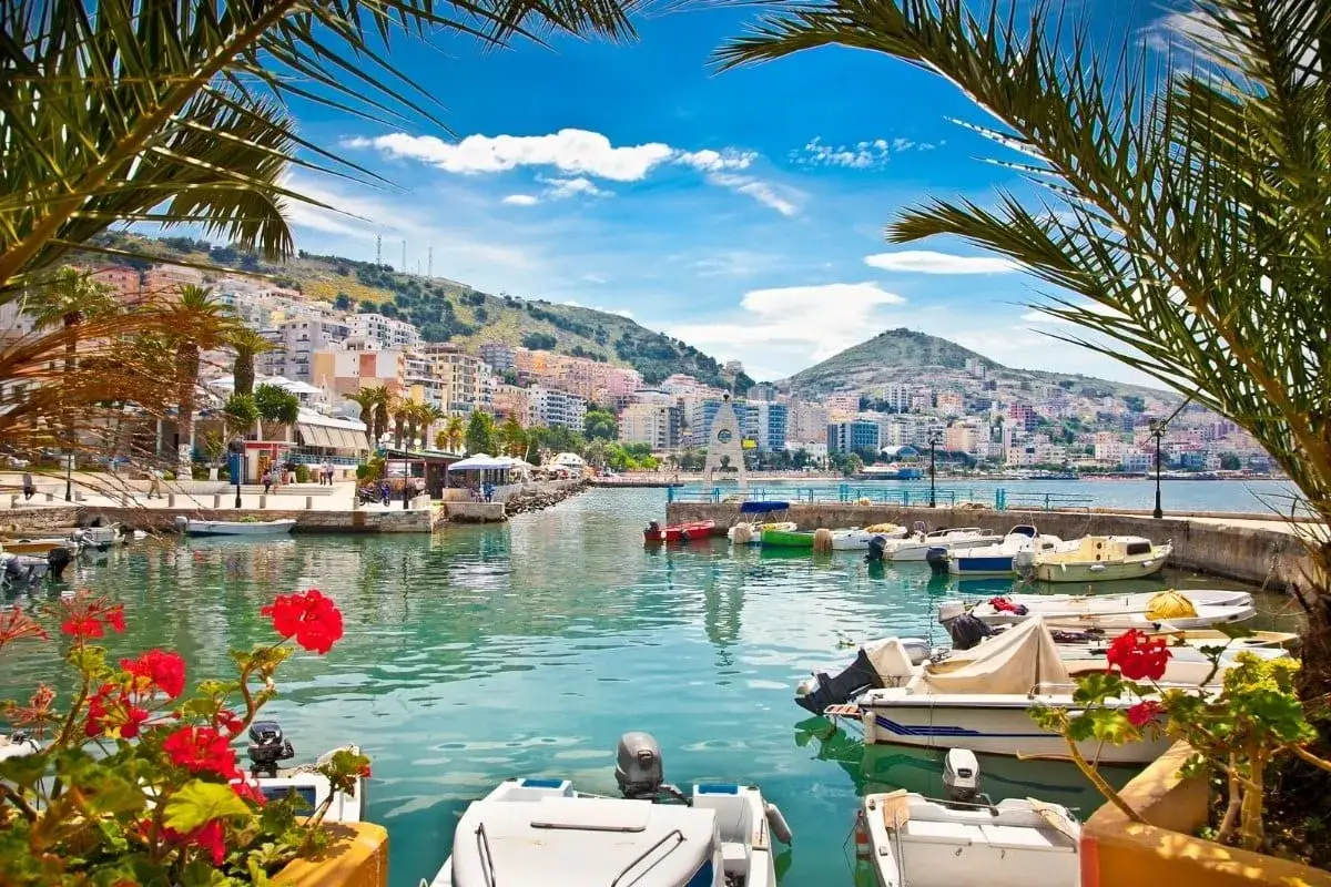 Malowniczy port w jednym z albania miasta turystyczne. Woda lśni, łodzie kołyszą się, a w tle widać kolorowe budynki na wzgórzu.