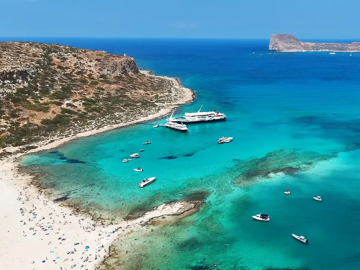 Rajska plaża z turkusową wodą, statkami i mnóstwem ludzi. Kreta wschodnia atrakcje zapierają dech w piersiach!
