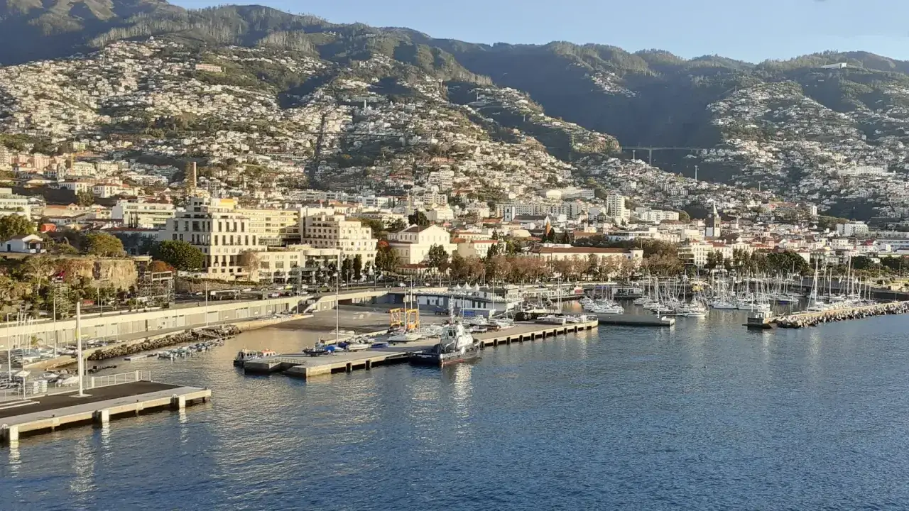 Widok na port z licznymi jachtami i statkami. W tle miasto Funchal na Maderze, z zabudowanymi zboczami gór. Może to być przystanek w podróży z Lizbony na Maderę promem.