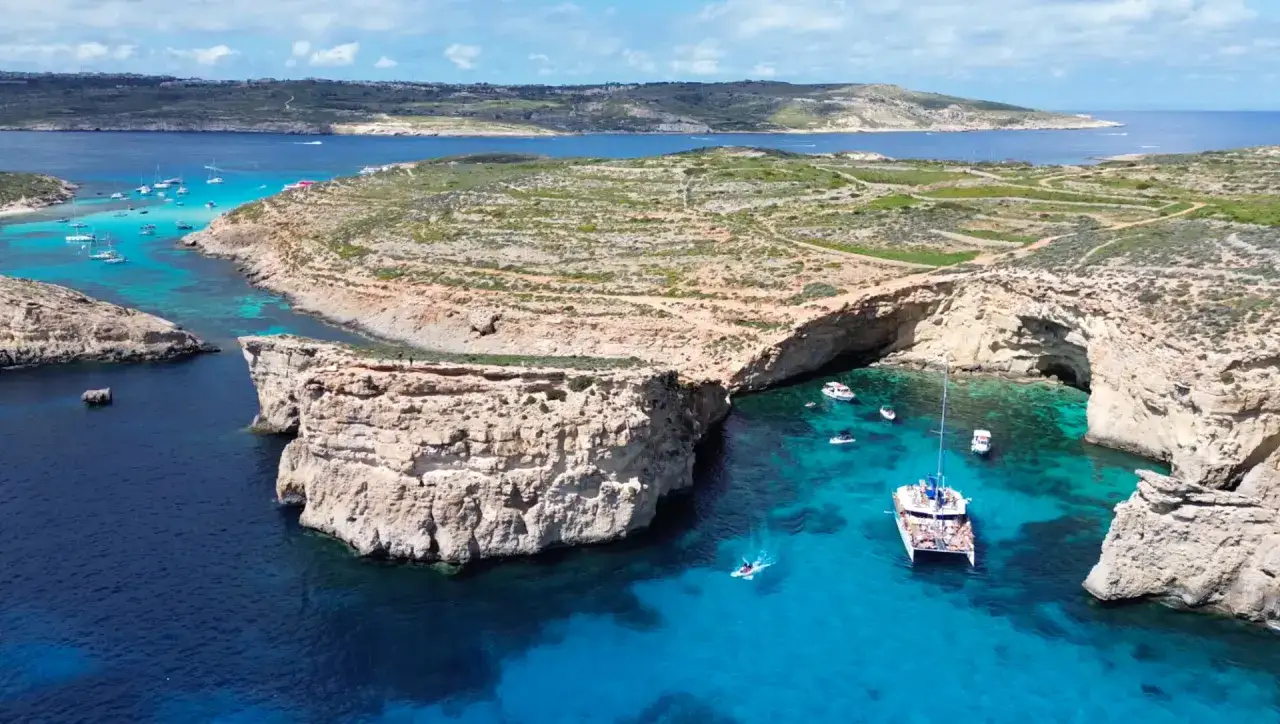 Malta co zobaczyć: Błękitna Laguna na Comino, z łodziami i klifami, to idealne miejsce na wakacje.