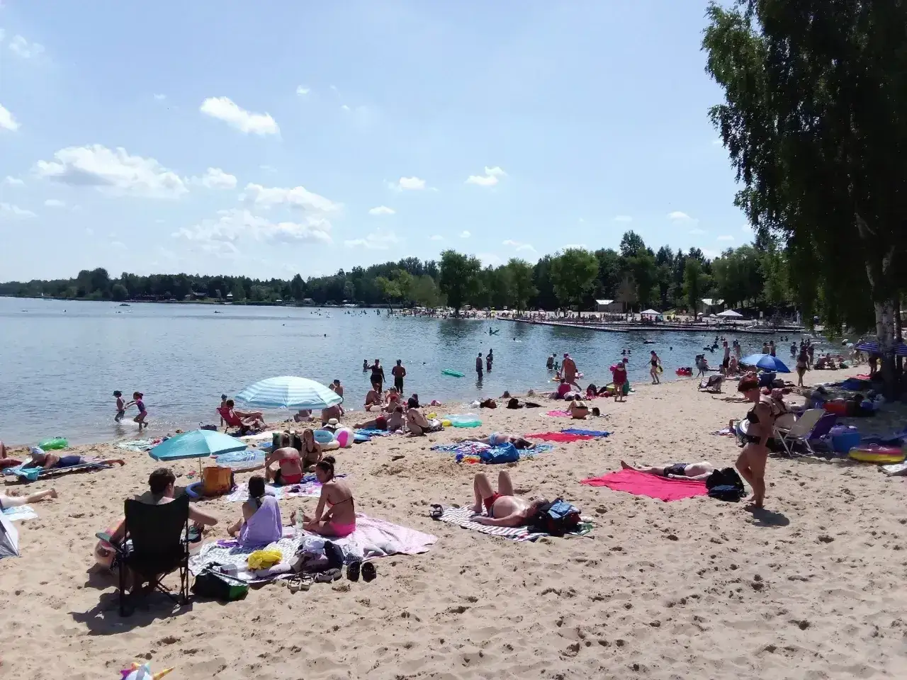 Słoneczny dzień nad jaworznem jeziorem. Ludzie odpoczywają na plaży, kąpią się i opalają.