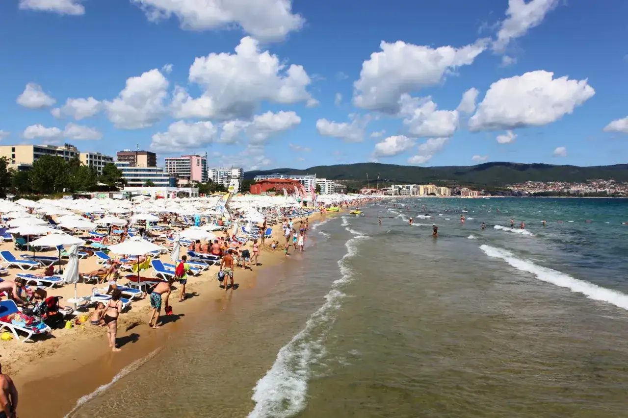 Słoneczny brzeg Bułgaria tętni życiem. Tłumy ludzi odpoczywają na plaży pod białymi parasolami, kąpią się w morzu i spacerują brzegiem.