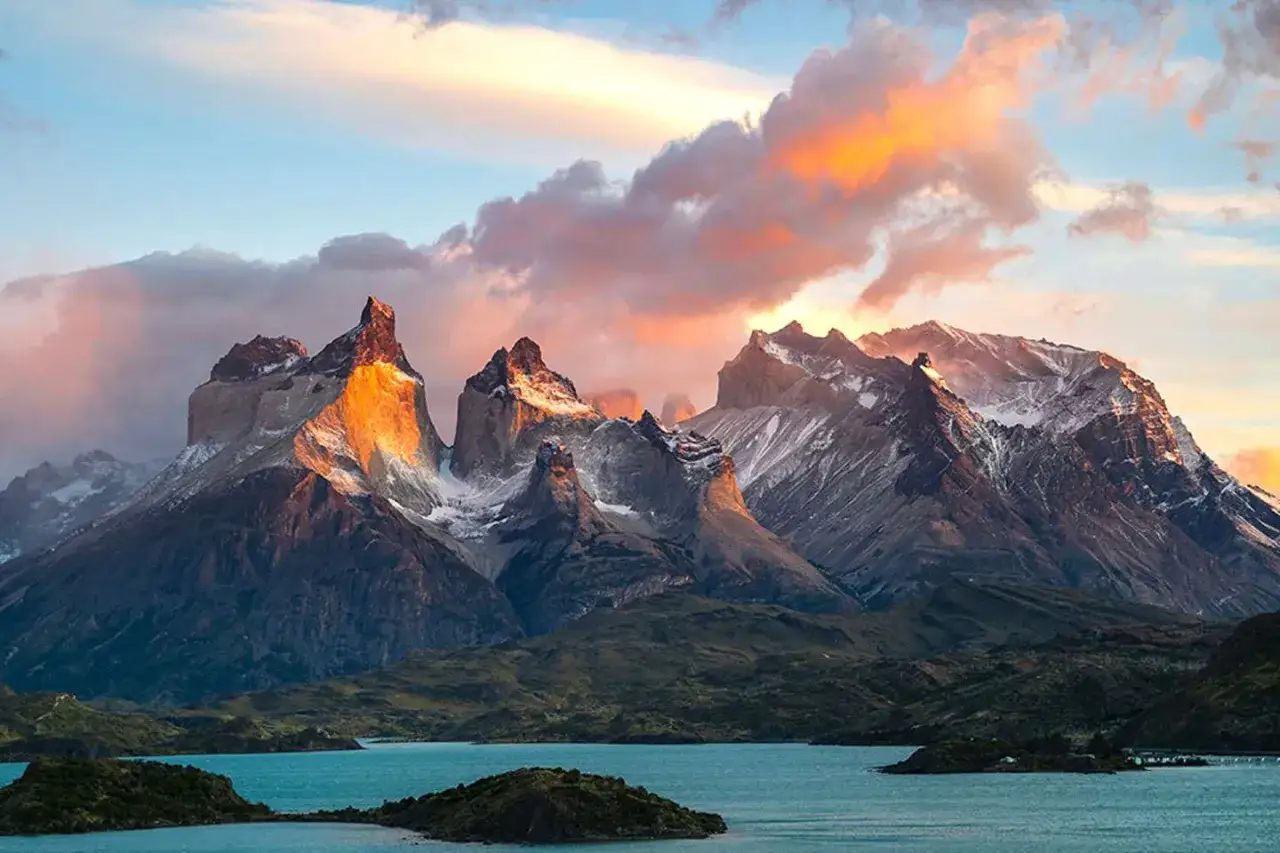 Majestatyczne szczyty Torres del Paine oświetlone zachodzącym słońcem, turkusowe jezioro i chmury malujące niebo. To obowiązkowy punkt na mapie, jeśli zastanawiasz się, co zobaczyć w Chile.