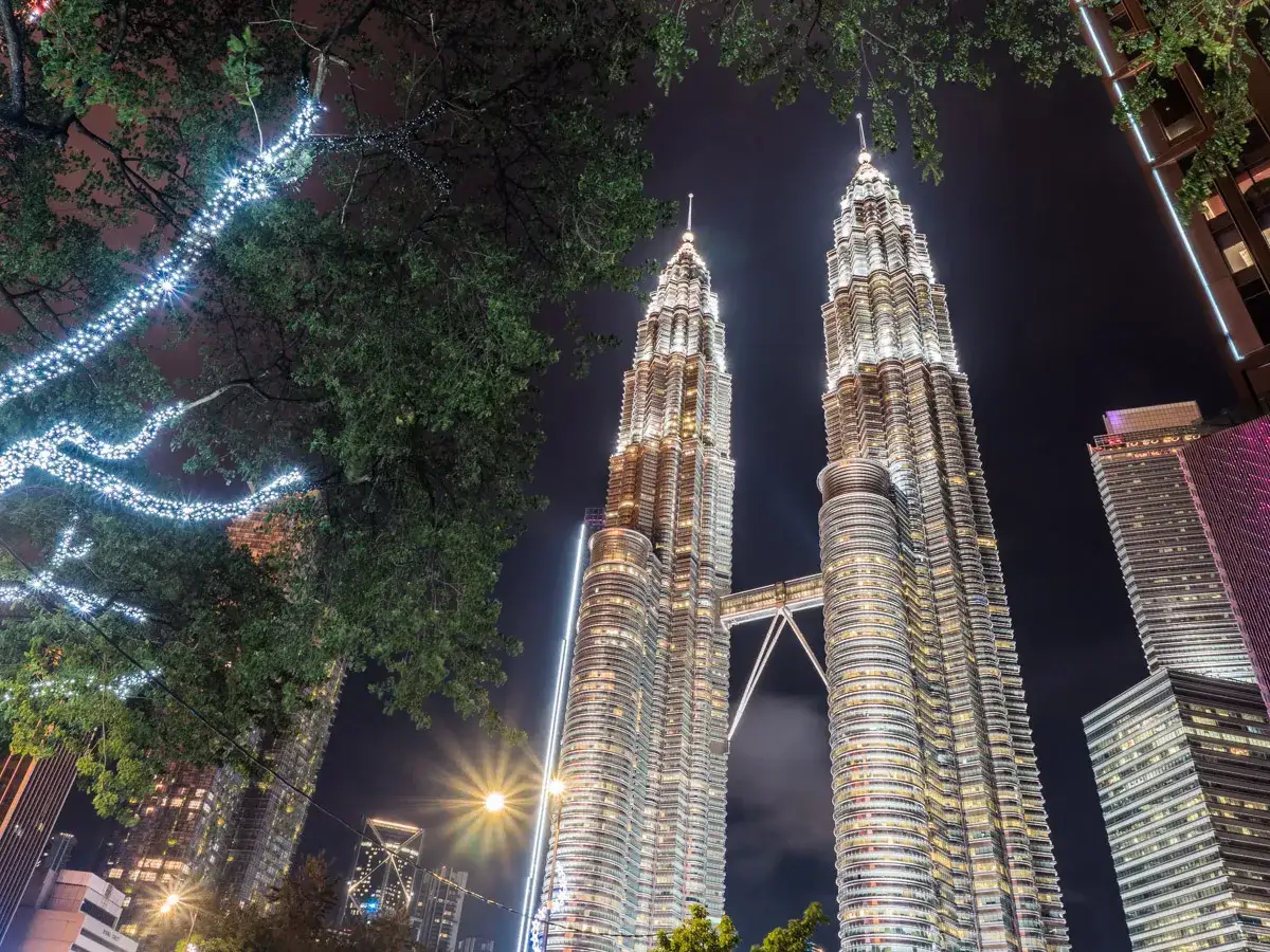 Wieżowce Petronas w Kuala Lumpur nocą, oświetlone i otoczone drzewami z lampkami.