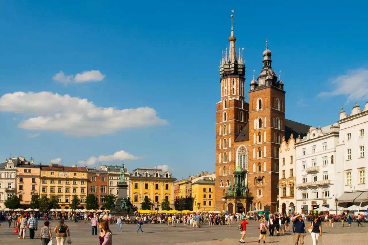 Rynek Gł&oacute;wny w Krakowie tętni życiem. W tle Bazylika Mariacka, a wok&oacute;ł kolorowe kamienice. Wiele ciekawostek o Krakowie czeka na odkrycie!
