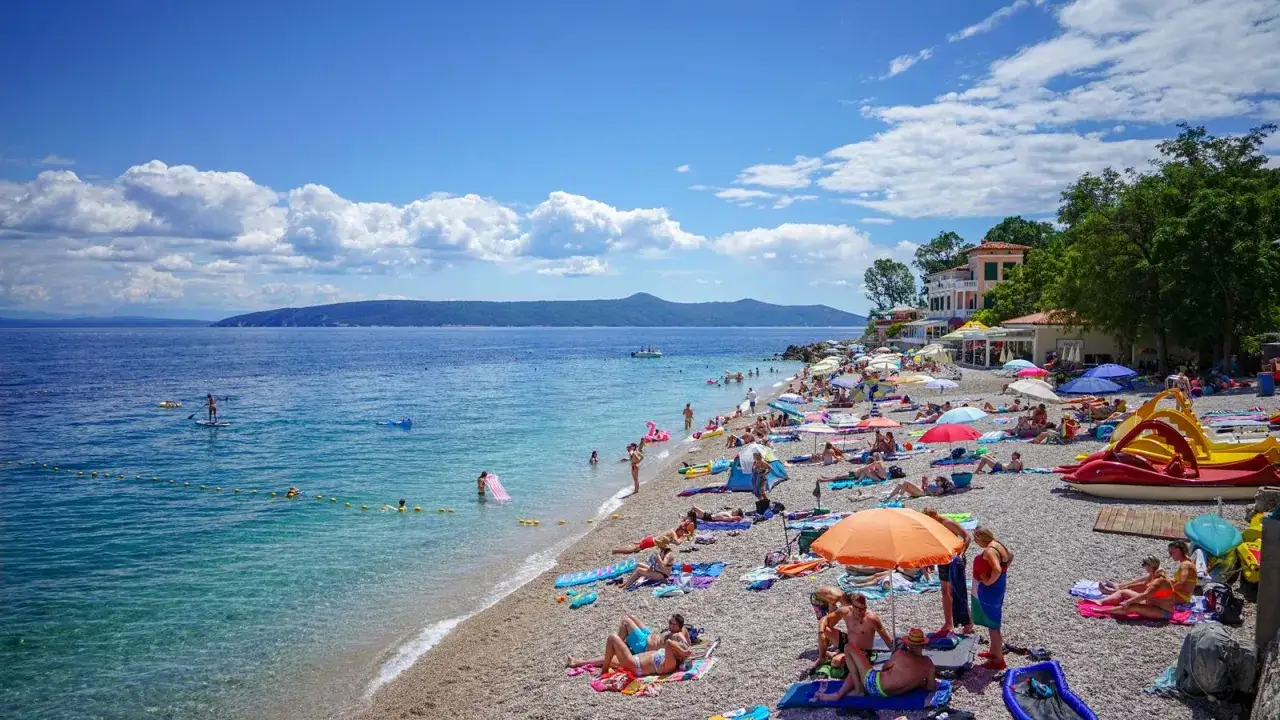 Słoneczny dzień na plaży na półwyspie Istria. Ludzie opalają się, pływają i relaksują pod parasolami.
